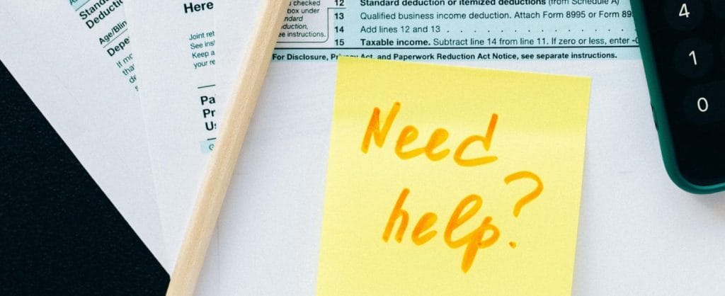 Simple photo with a 1040 tax form showing in the background. Post it on front says, "need help?"